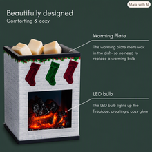 Load image into Gallery viewer, White brick fireplace‑style wax warmer with glowing LED embers and three holiday stockings hanging across the front. Cream wax cubes sit on the warming plate on top. Text beside the warmer highlights its design, warming plate, and LED glow features.
