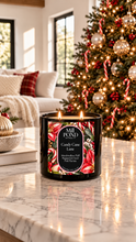 Load image into Gallery viewer, “Lit black candle labeled Candy Cane Lane sitting on a marble table in front of a decorated Christmas tree with red and white candy canes, red ornaments, silver baubles, and a cozy living room with a white couch and holiday pillows in the background.”
