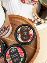 Load image into Gallery viewer, Two Mill Pond Candle Co. tins on a wooden tray, one labeled Fresh Coffee and the other Wild Berry Croissant, with a candle and a mug in a styled setting.
