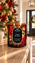Load image into Gallery viewer, Brown glass three‑wick candle burning on a wooden surface with a festive holiday label that reads Mill POND Candle Co., Tinsel &amp; Time, Ruby Pomegranate, Crisp Juniper, Apple &amp; Sage. Surrounding décor includes red poinsettias, golden bells, greenery, and a softly lit Christmas tree in the background.”
