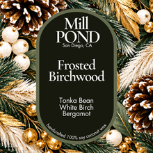 Load image into Gallery viewer, “Green candle label reading Frosted Birchwood, surrounded by pinecones, evergreen branches, and gold and white ornaments.”
