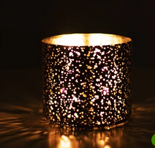 Load image into Gallery viewer, A cylindrical black candle holder or lamp with a glittery, speckled cutout pattern, glowing warmly from within against a dark background.
