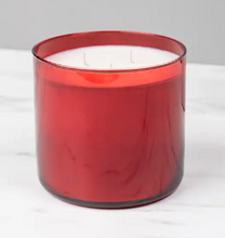 Load image into Gallery viewer, A red translucent glass jar candle with white wax and three wicks, set against a neutral gray background on a light marble surface.

